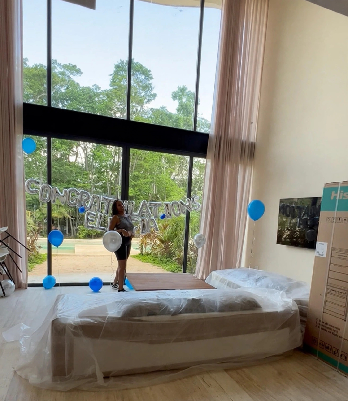A client standing by tall villa windows with silver congratulations letter balloons and blue balloons