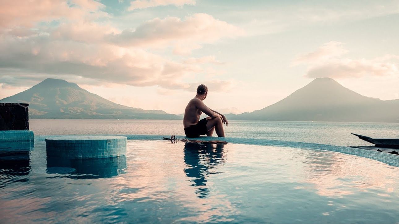 Traveler seated by an infinity pool with lake and mountain views in Guatemala