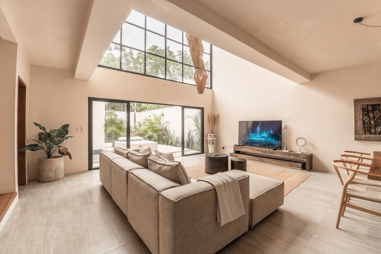 Bright living room with tall windows, beige sectional sofa, and TV at the four-bedroom villa in Mexico