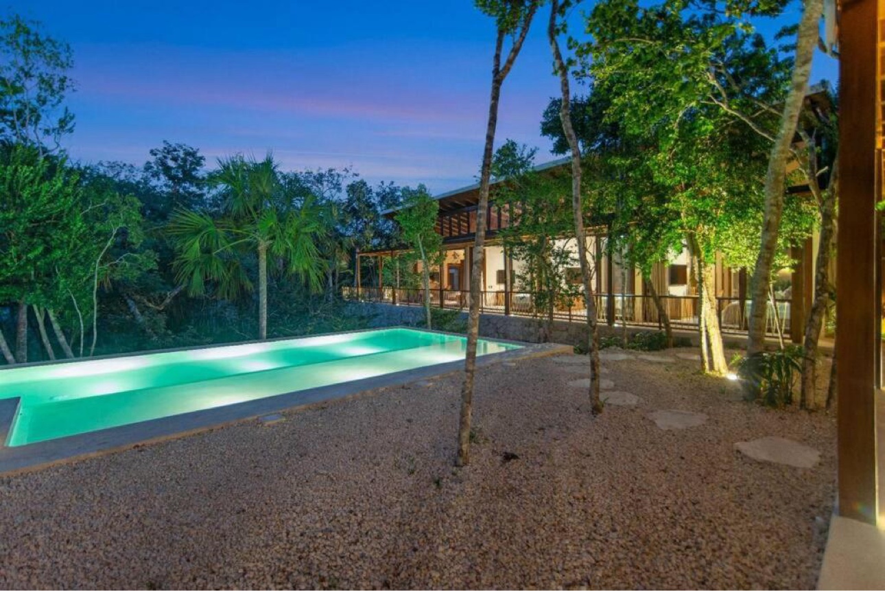 Glowing turquoise pool at dusk with the four-bedroom villa and surrounding trees in Mexico