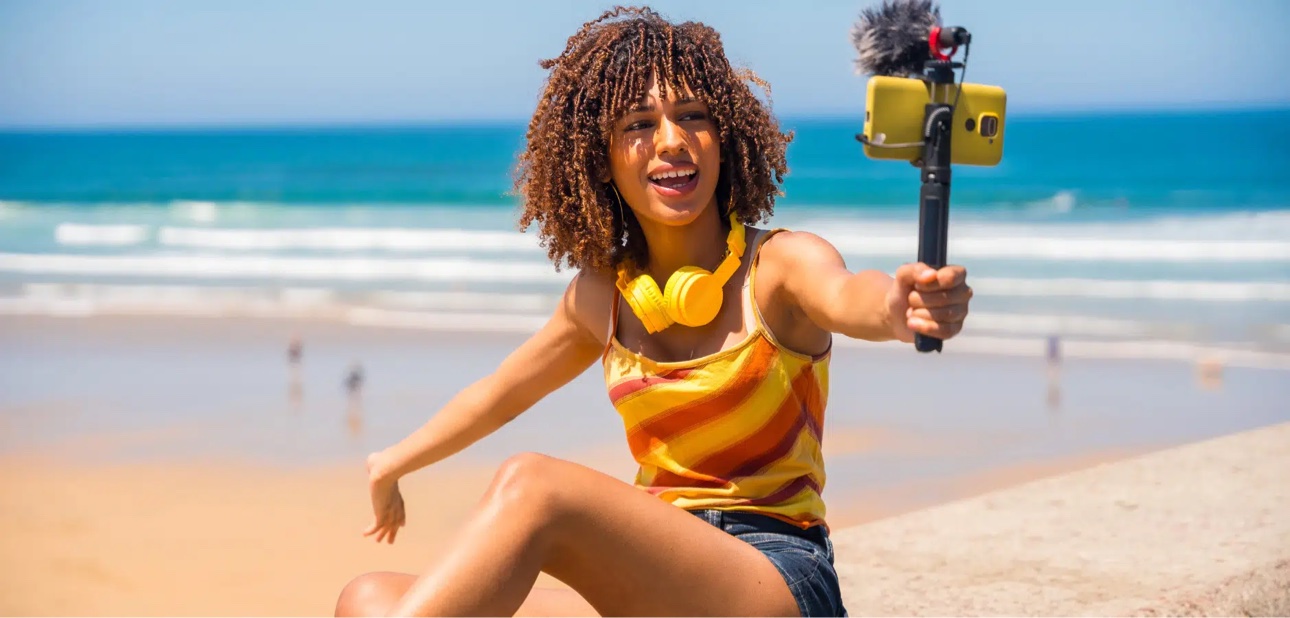 Young content creator filming herself with a phone on a selfie stick at the beach
